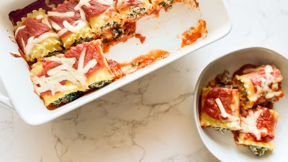 Pesto Lasagna Rolls topped with melted cheese and fresh basil in a baking dish