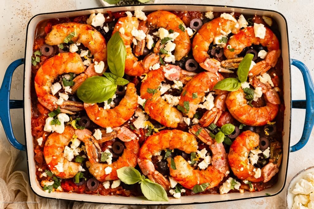 Shrimp Saganaki in a skillet with tomato sauce and crumbled feta, garnished with parsley.