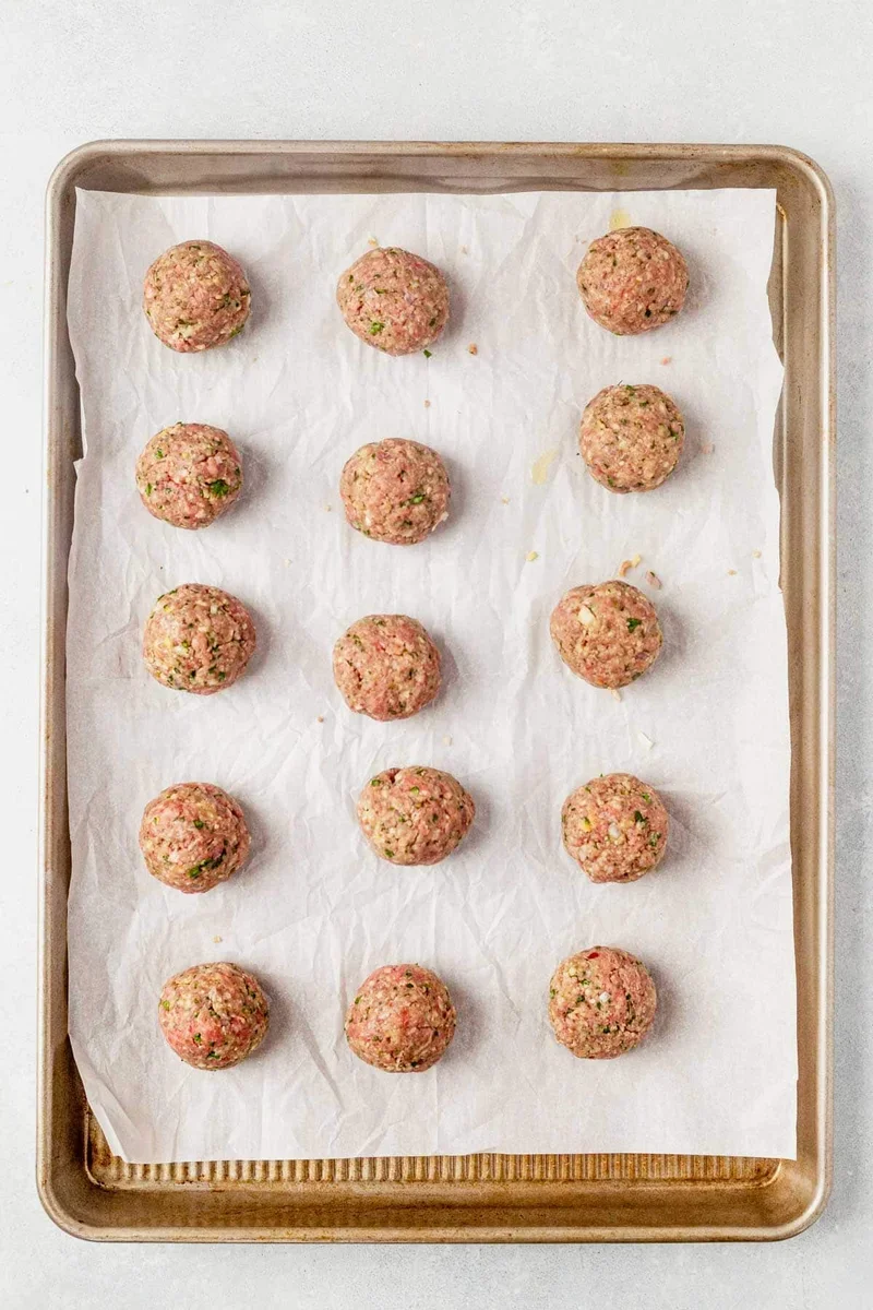 evenly sized raw meatballs arranged on cutting board before cooking