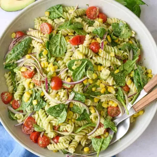creamy avocado pasta salad with tomatoes and corn in a white bowl
