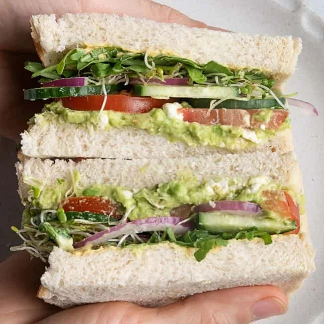 fresh avocado sandwich ingredients including tomato, cucumber, and sprouts on cutting board