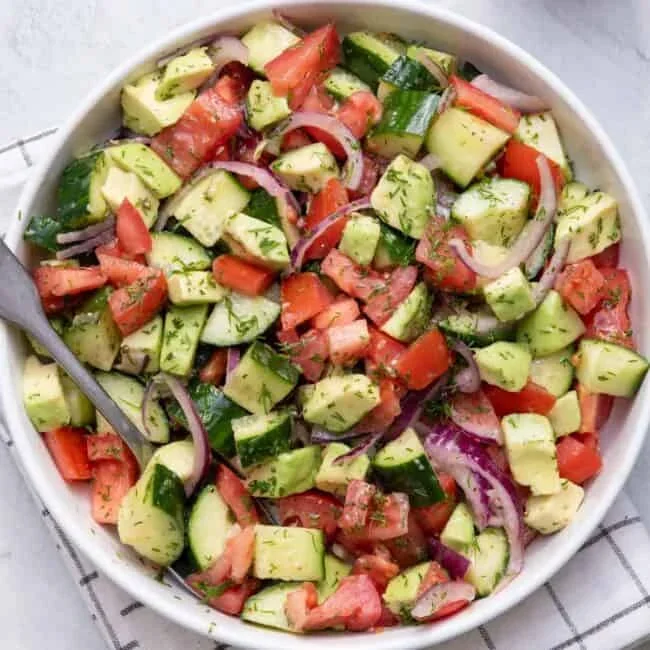 vibrant tomato cucumber avocado salad in a white bowl with dill garnish