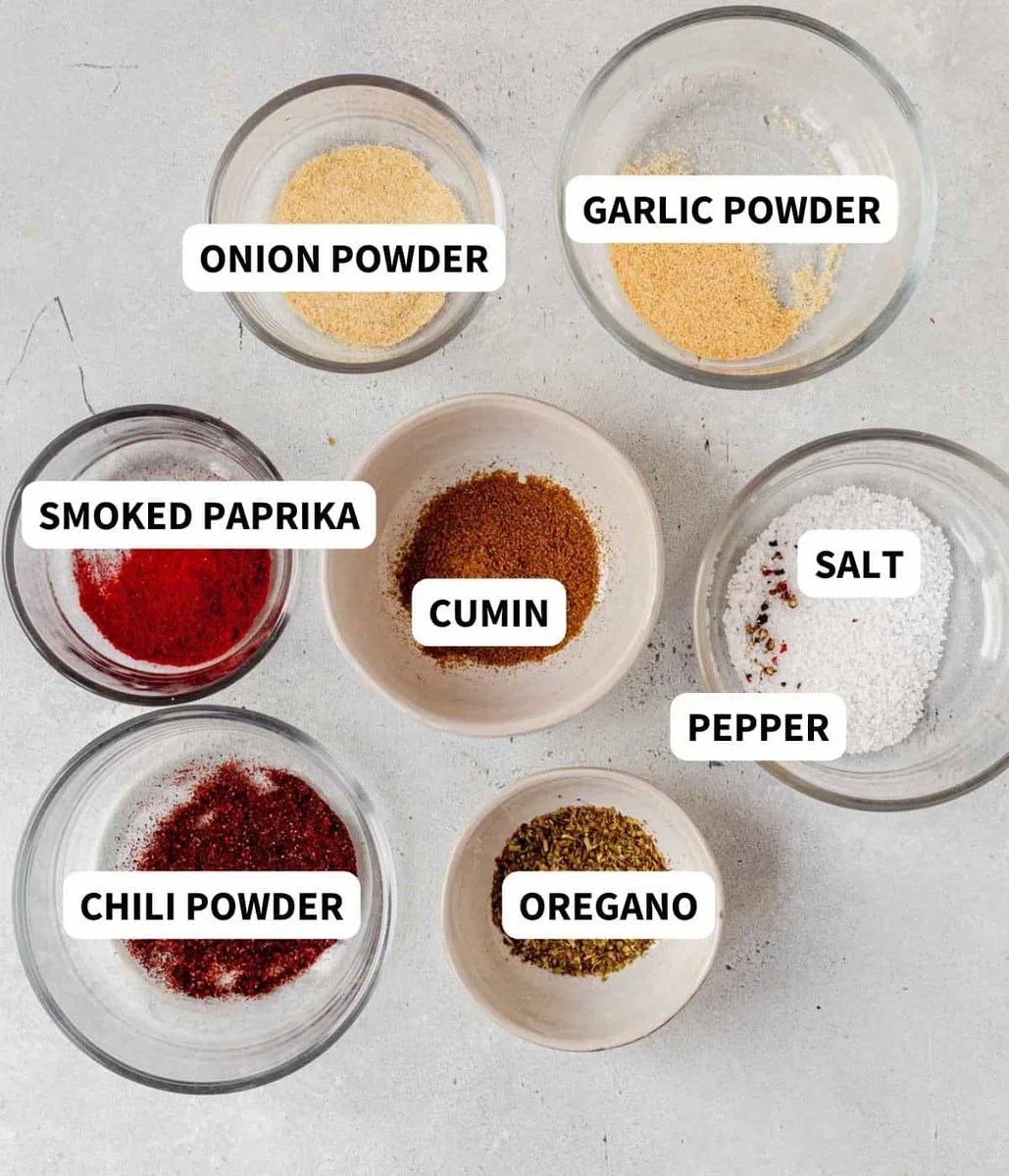 carnitas seasoning ingredients including cumin, oregano, and smoked paprika in small bowls
