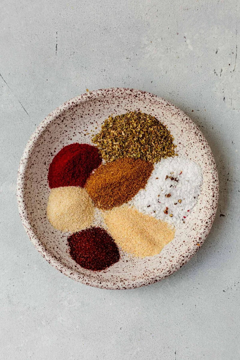 measuring spoons with cumin and chili powder for homemade carnitas seasoning