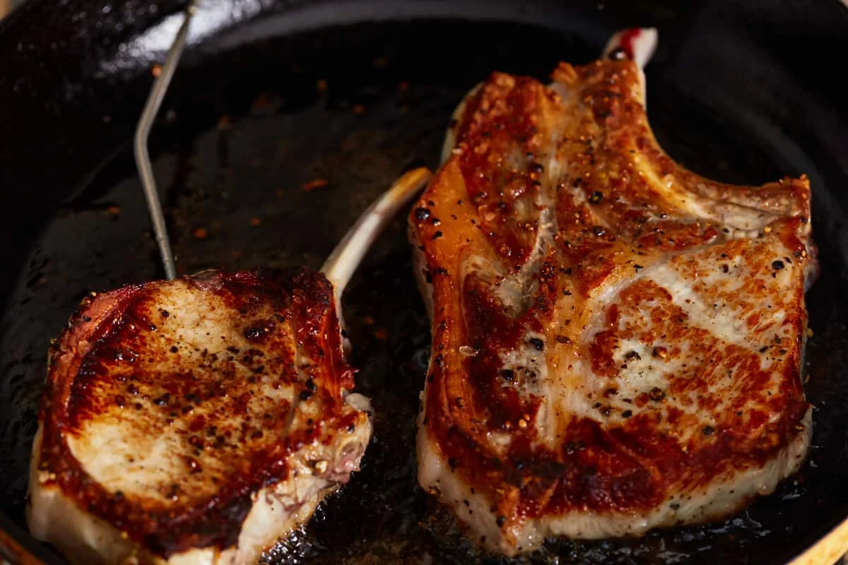 Cast Iron Pork Chops Recipe - The Cookie Rookie® 6 pork chops sizzling in hot cast iron skillet with golden crust