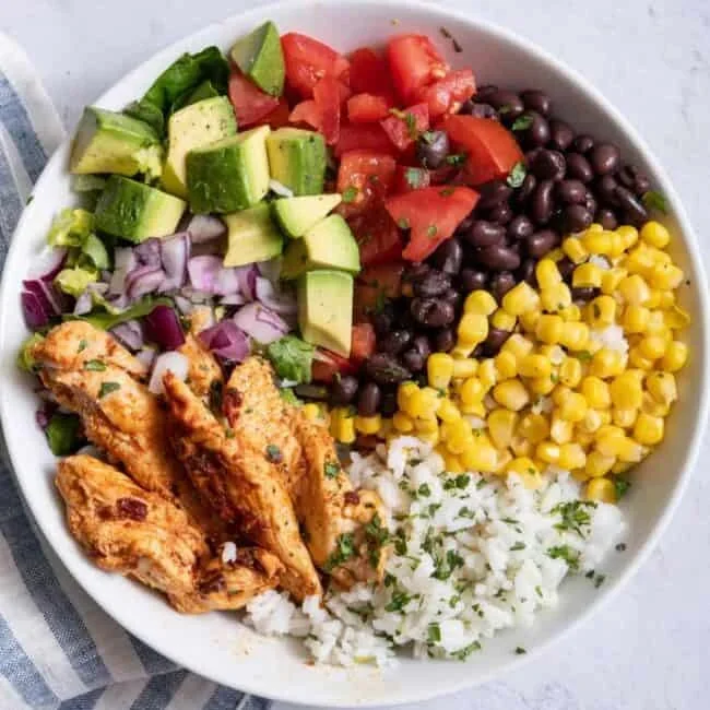 assembled chicken burrito bowl with rice, black beans, corn, and avocado crema