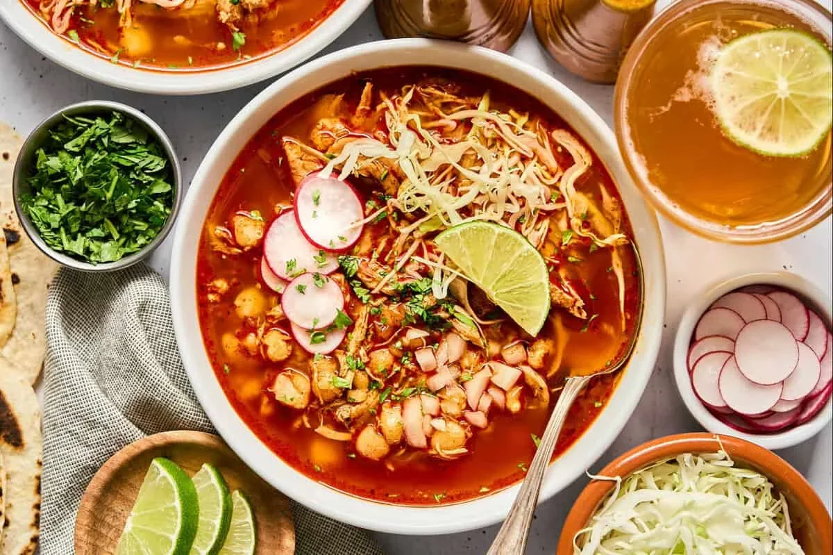bowls of red chicken pozole topped with cabbage, radishes, cilantro and lime