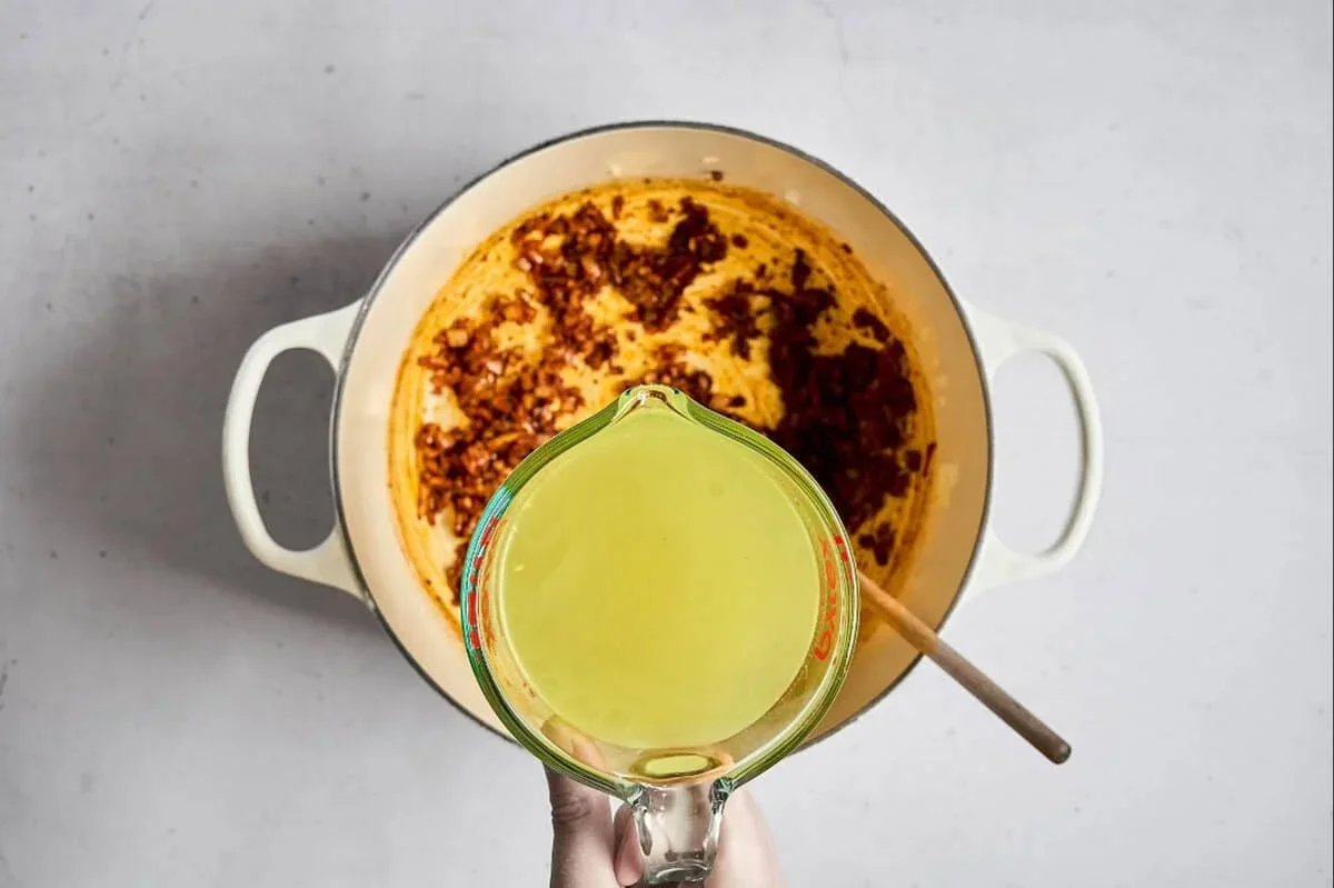 chicken pozole rojo broth boiling in a dutch oven with red chili foam