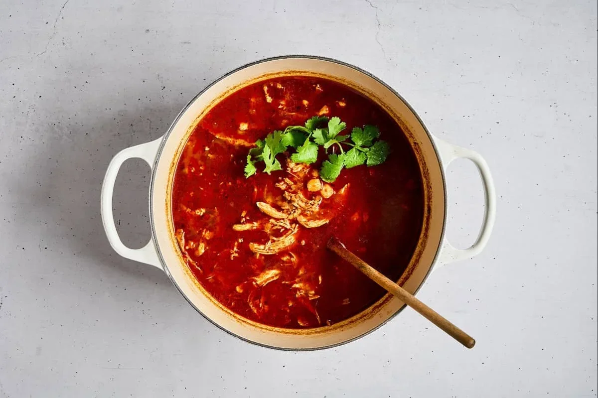 tasting chicken pozole rojo with a spoon in the pot