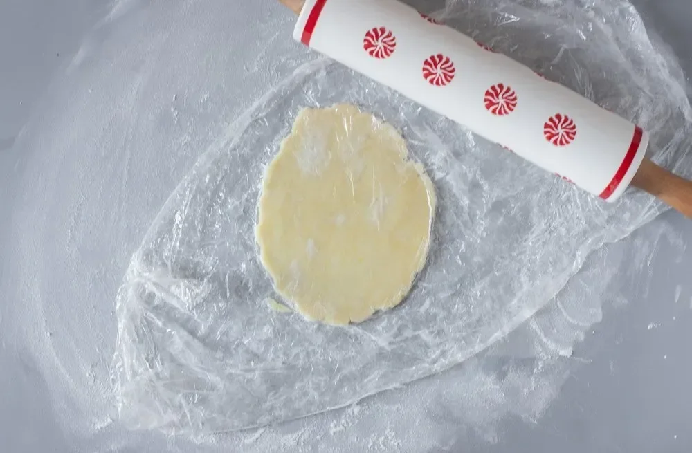 rolling gluten-free cookie dough between parchment paper with date filling visible