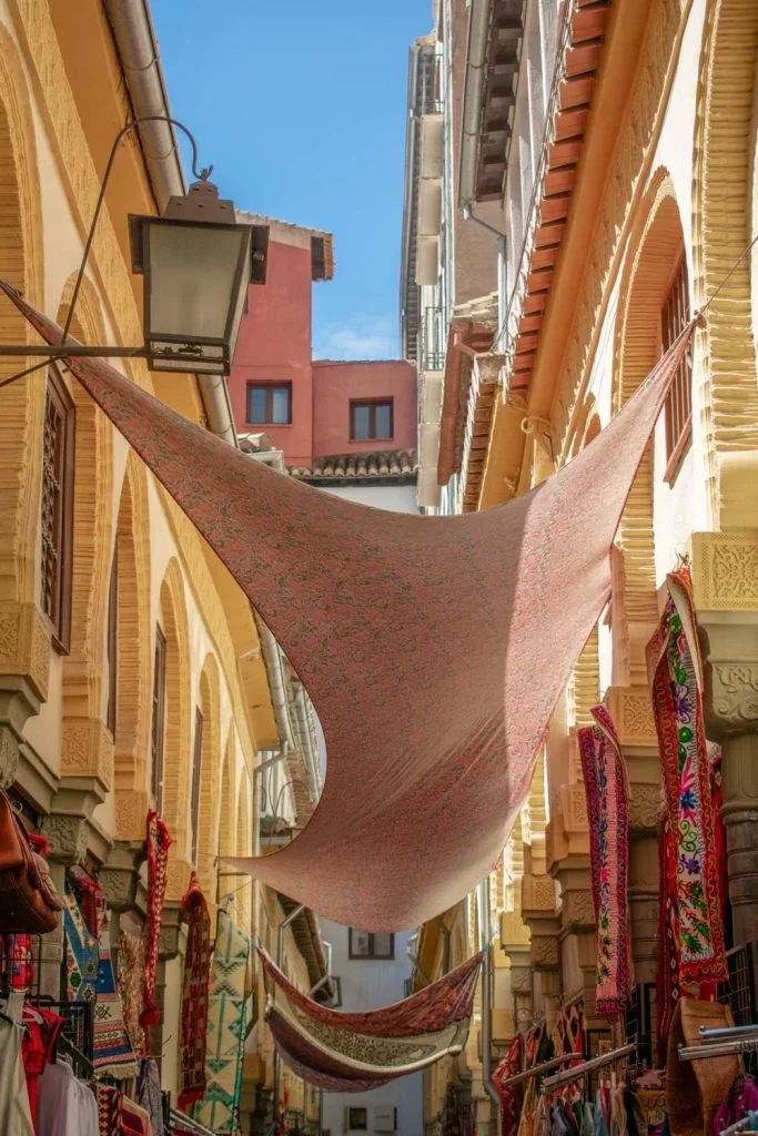 Narrow alley in Granada's Alcaicería market with colorful textiles and crafts