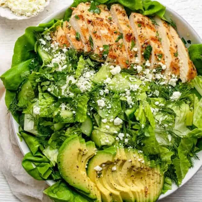 vibrant green goddess salad with creamy yogurt dressing in a white bowl