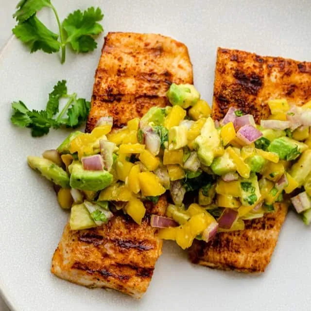 Grilled mahi mahi topped with colorful mango avocado salsa on a white plate