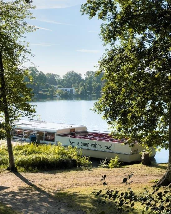 A red sightseeing boat cruising on a calm lake in Plön surrounded by green forests