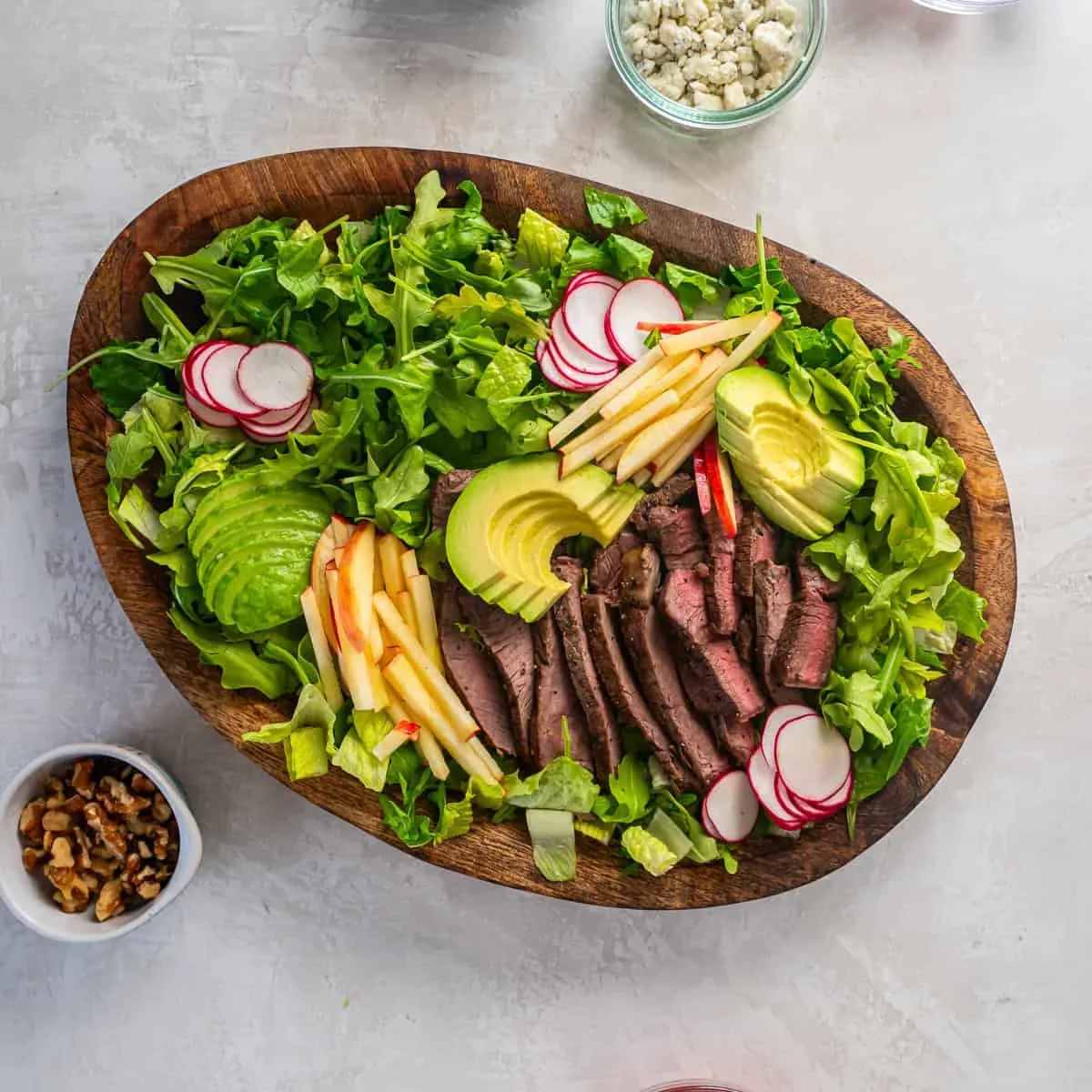 avocado, apple, and radish arranged around steak on salad