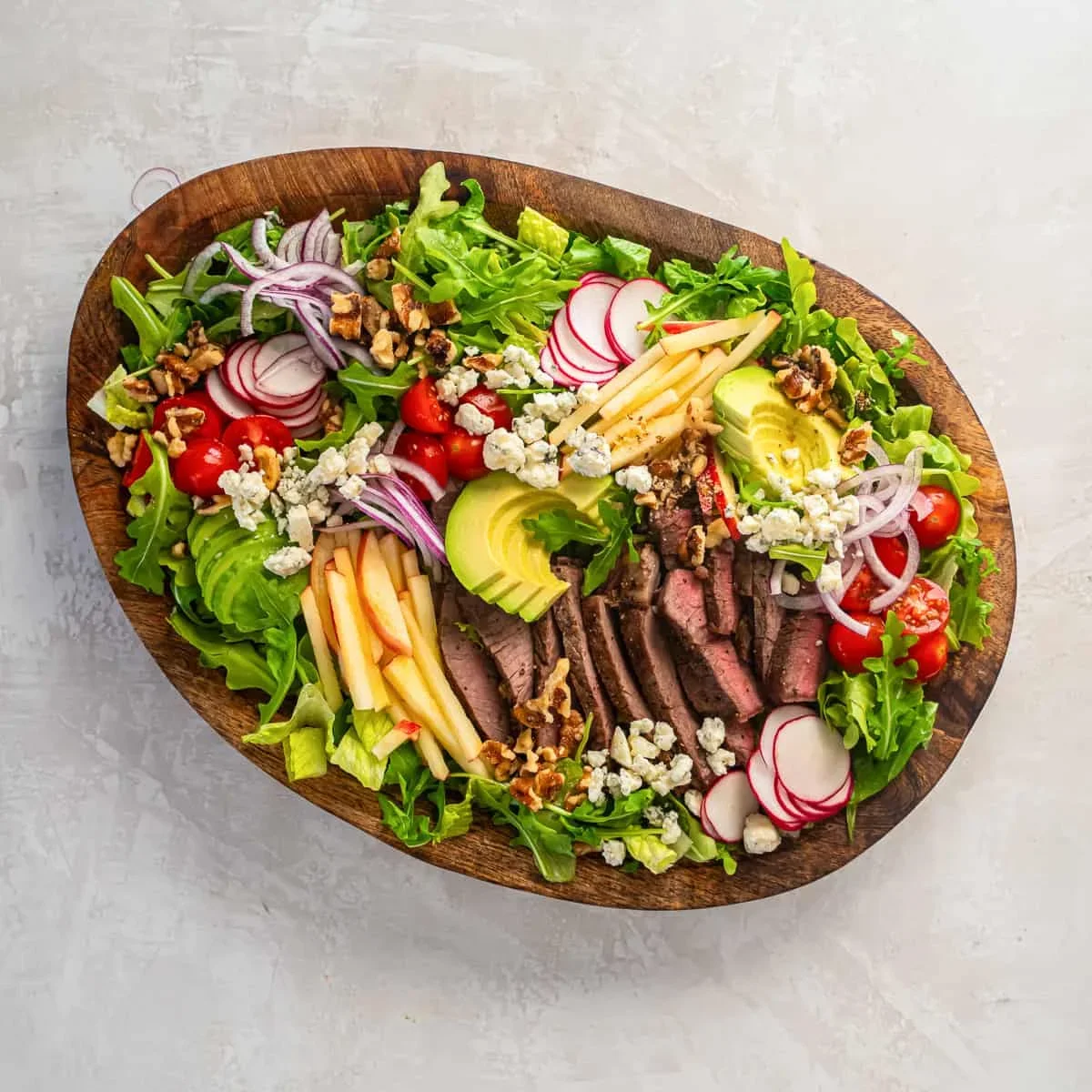 blue cheese crumbles and walnuts being added to steak salad