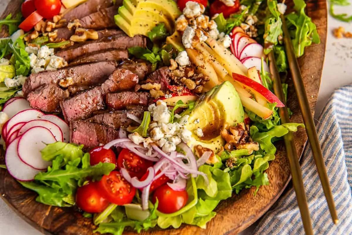 steak salad ingredients separated in meal prep containers with avocado and walnuts