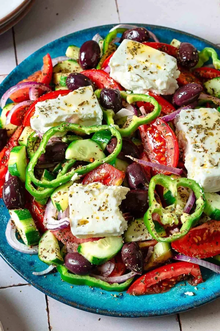 fresh greek salad ingredients including tomatoes, cucumber, olives, and whole feta block