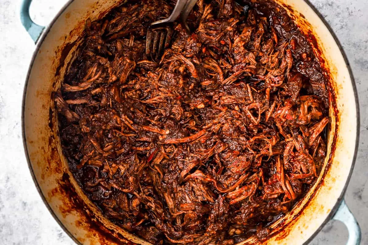 beef and short ribs slow cooking in birria sauce in a covered dutch oven