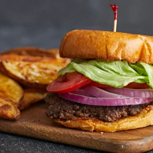 Easy Smash Burger Recipe with Crispy Edges in 30 Minutes 2 assembled smash burger with cheese and toppings on a toasted bun