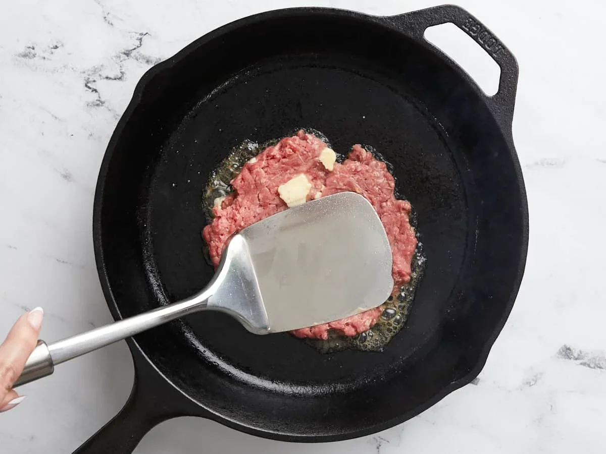 Easy Smash Burger Recipe with Crispy Edges in 30 Minutes 7 pressing smash burger patty thin with spatula in cast iron